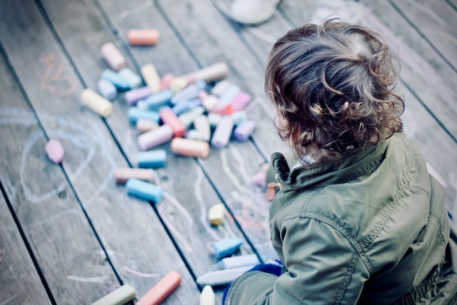 Ein Kind, dass smit Kreide auf einen Holzboden malt.